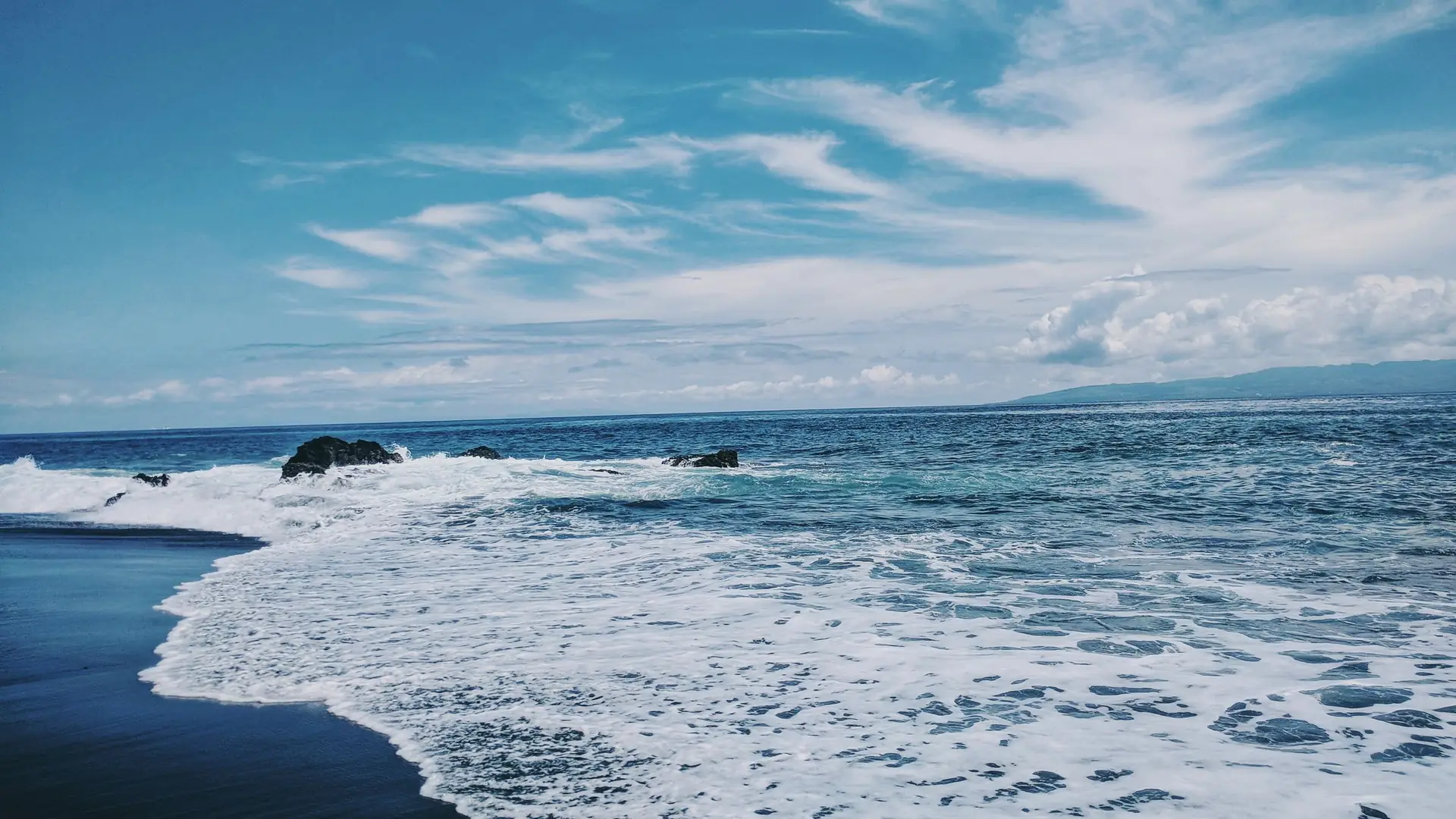 Foamy waves on a black-sand shore under a blue sky