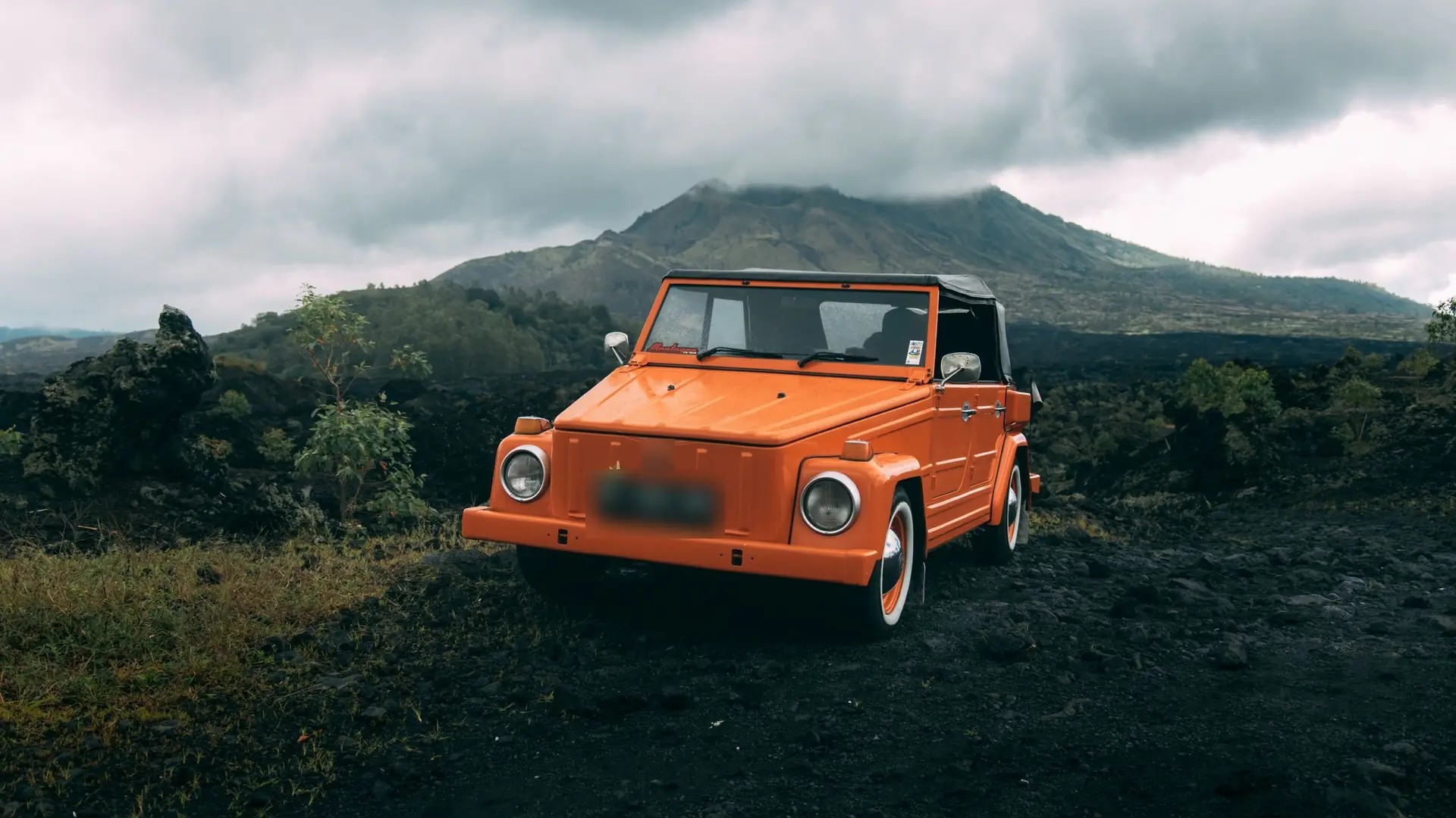 An orange open-top car parked on a volcanic landscape in Bali