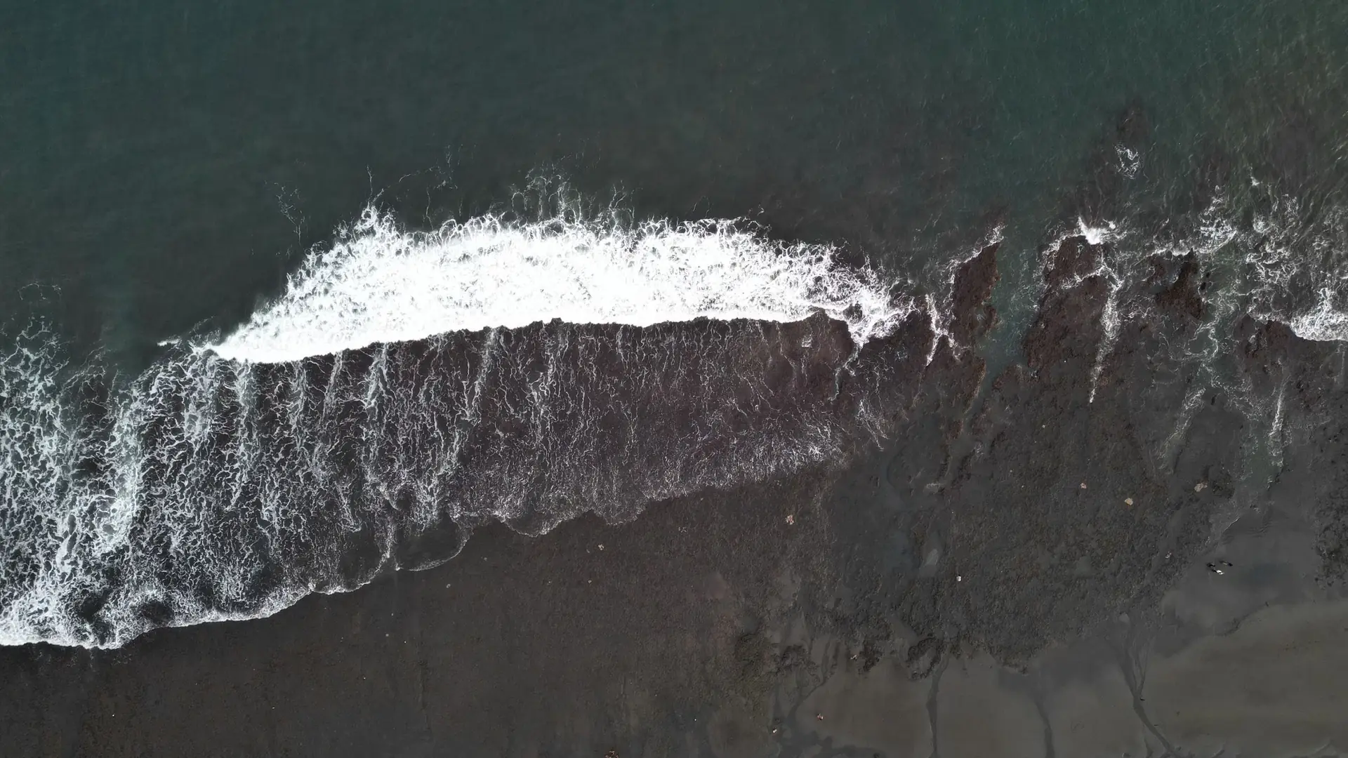 Aerial view of white surf breaking on dark volcanic sand