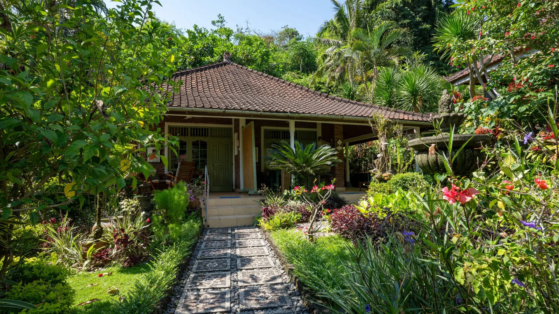 A small Balinese house with a stone path through a flowering garden