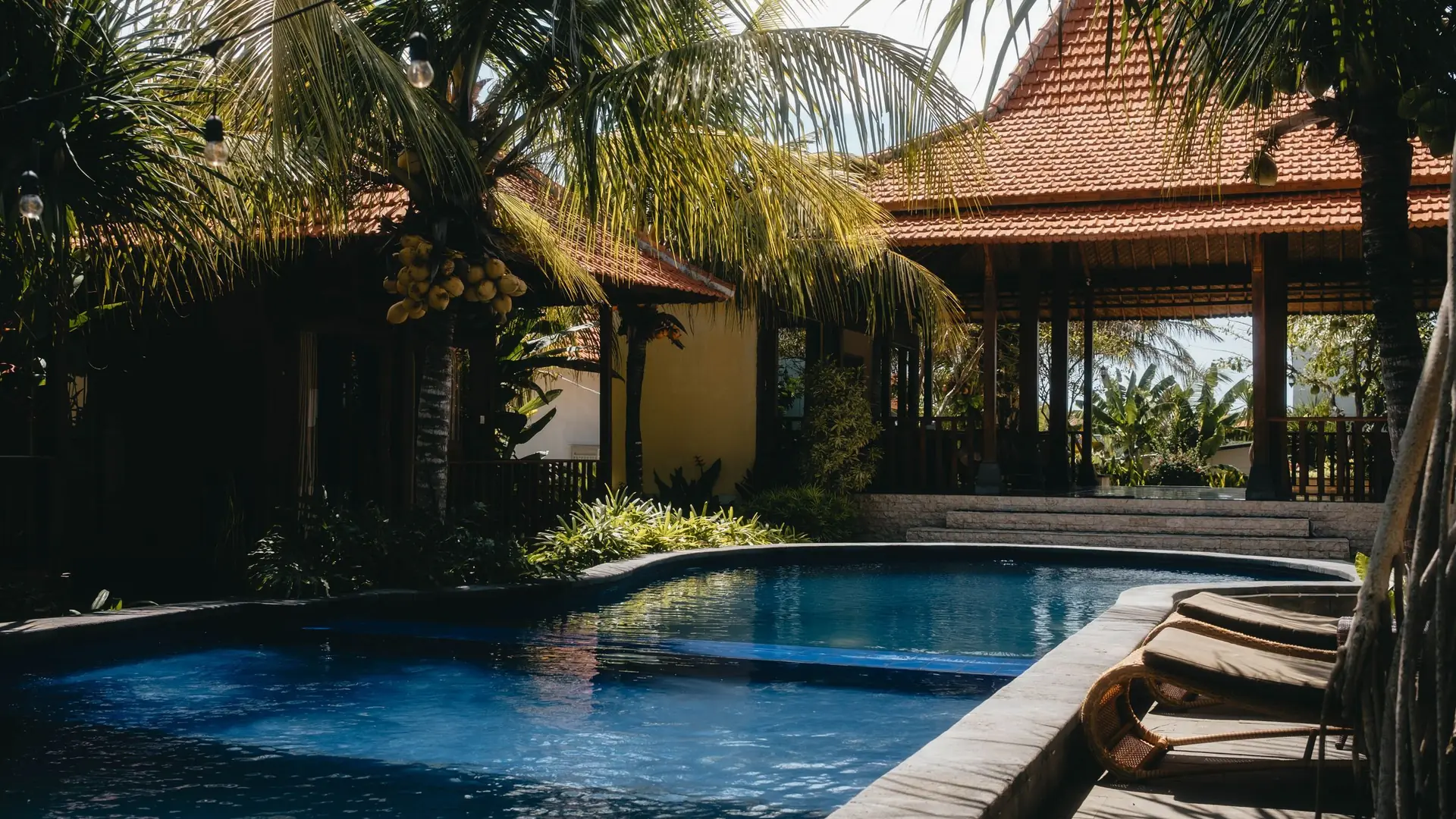 A swimming pool beside a Balinese pavilion with palm trees