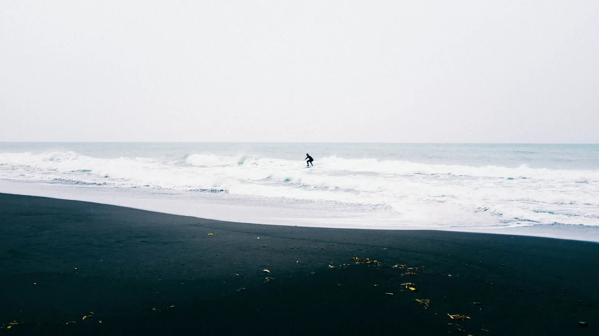 A distant surfer in the waves off a black-sand beach